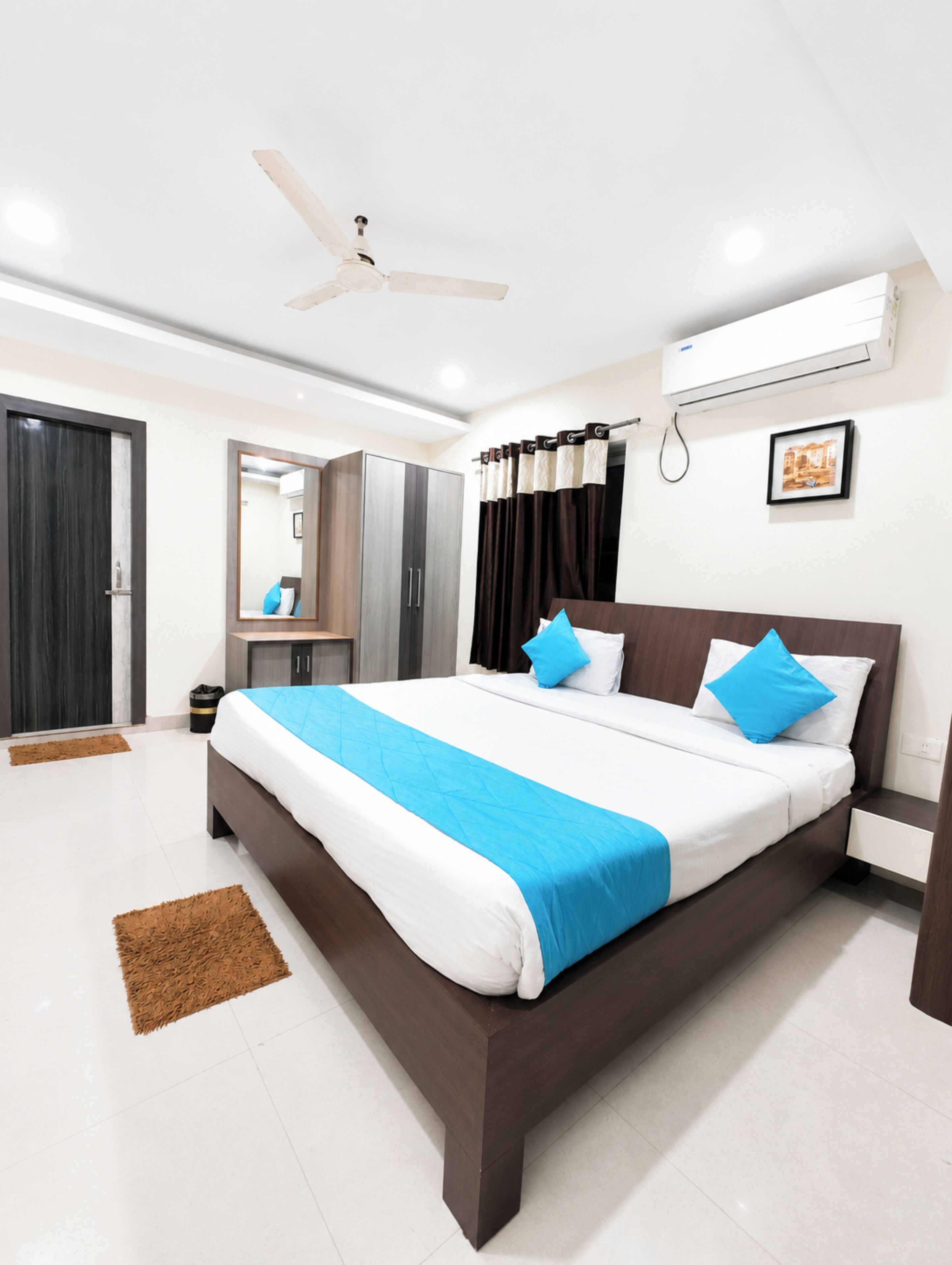 A modern bedroom with a large bed, a ceiling fan, an air conditioning unit, a mirror, and a framed picture on the wall.