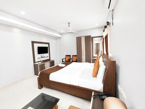 A modern hotel room with a large bed, a flat-screen TV, a desk with a chair, a wardrobe, and a mirror. - Hotel Corbett Fun Resort  (Ramnagar)