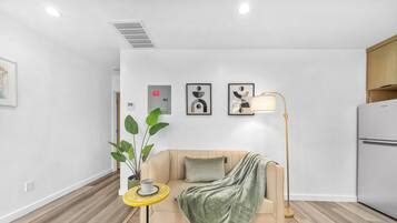 A modern living room with a sofa, a floor lamp, a potted plant, and framed artwork on the wall.