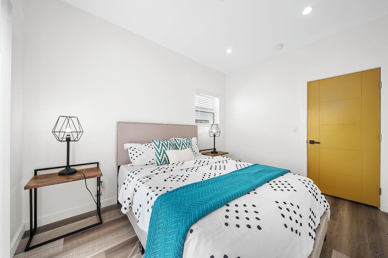 Un dormitorio con cama, mesita de noche, lámpara, ventana y puerta.