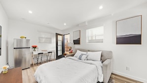 A modern bedroom with a large bed, a desk, and a refrigerator. - The Urban Suites (Los Angeles)