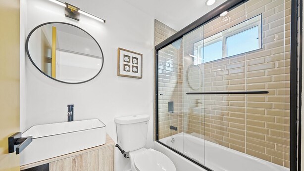A modern bathroom with a white toilet, a glass-enclosed shower, a round mirror, and a white sink.