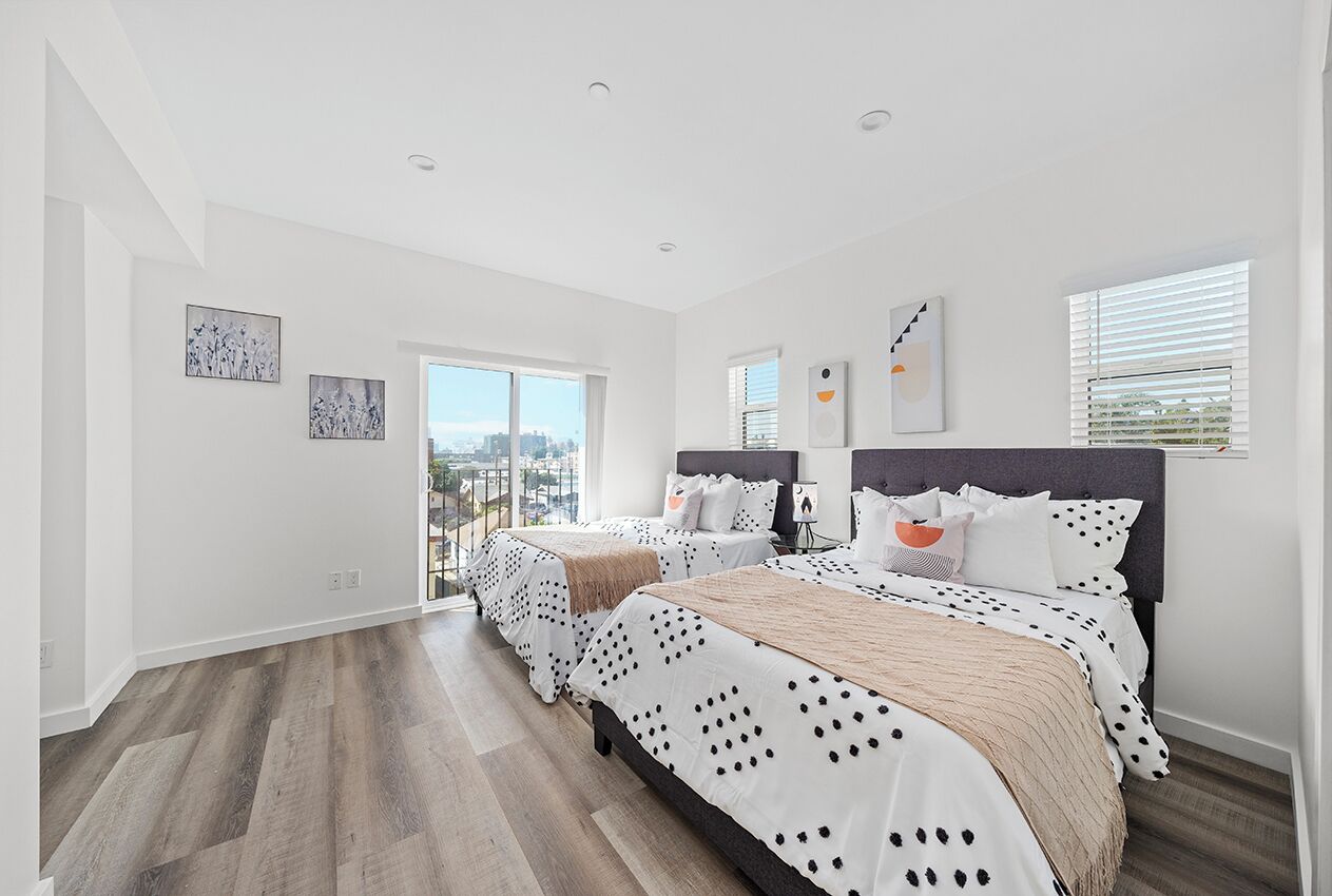 Ein modernes Schlafzimmer mit zwei Betten, großen Fenstern und Blick auf die Stadt.