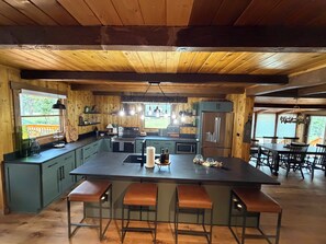 A modern kitchen with a central island, bar stools, a dining area with a large table, and a view of the outdoors. - 3-bedroom Cabin in Seeley Lake MT (Seeley Lake)