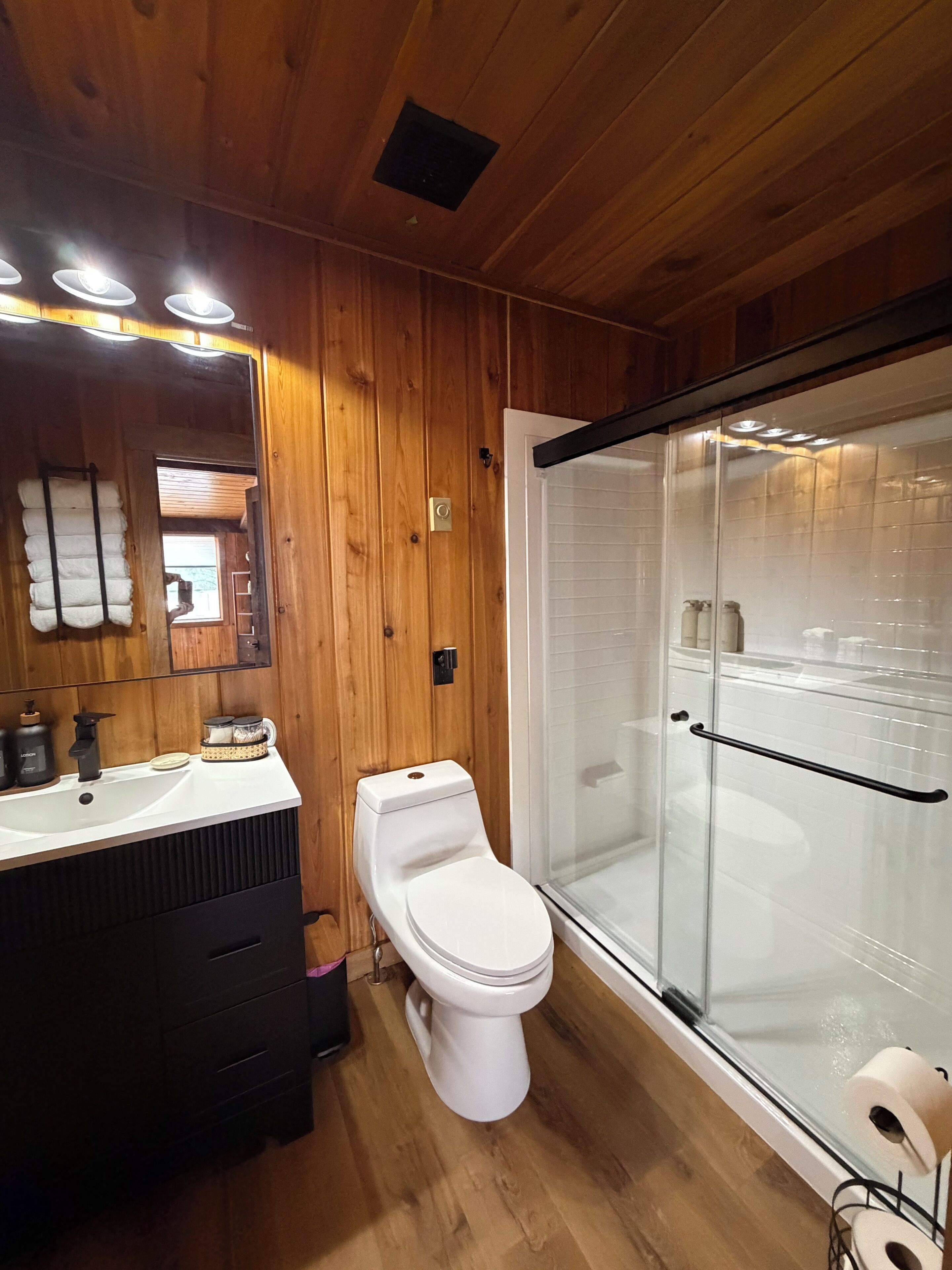 A wooden-paneled bathroom with a white sink, a toilet, and a glass-enclosed shower.