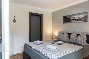 Ein Schlafzimmer mit einem Bett, einer Tür, einer Wandleuchte, einem Bild und einer Heizung.