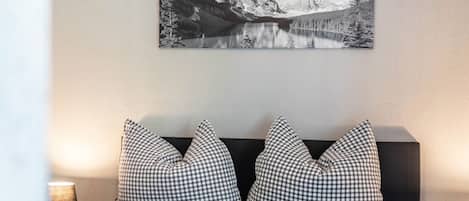 A bedroom with a bed, checkered pillows, a mountain landscape painting, and a lamp.