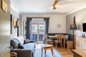 A cozy living room with a sofa, a dining table, and a TV mounted on the wall. - Apartment 'Kuhglocken' with Mountain View, Shared Garden and Wi-Fi (Döbriach)