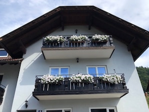 Ein mehrgeschossiges Gebäude mit Balkonen, die mit Blumen geschmückt sind, einem geneigten Dach und einer weißen Fassade.