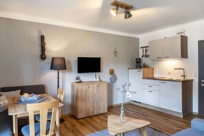 Ein kompakter Wohnraum mit Essbereich, einer Couch, einem Fernseher, einem Holzschrank und einer Küchenzeile.