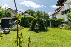 Ein gepflegter Garten mit Rasenfläche, einer Pergola und unterschiedlichen Pflanzen.