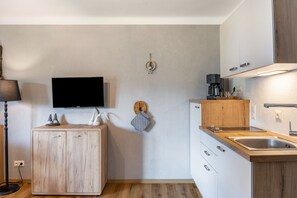 A modern kitchen with wooden cabinets, a built-in oven, a coffee maker, and a flat-screen TV mounted on the wall. - Apartment 'Kuhglocken' with Mountain View, Shared Garden and Wi-Fi (Döbriach)