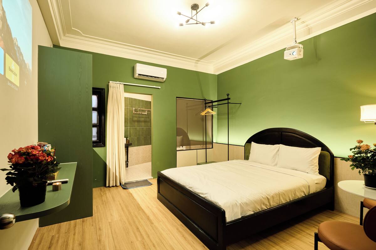 Ein Hotelzimmer mit Bett, Schreibtisch, Spiegel, Dusche und einer grünen Wand.