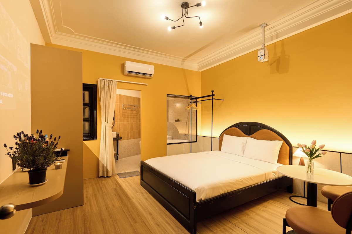 Ein Hotelzimmer mit Bett, einem kleinen Tisch, einem Sessel, einer Topfpflanze und einer Dusche.