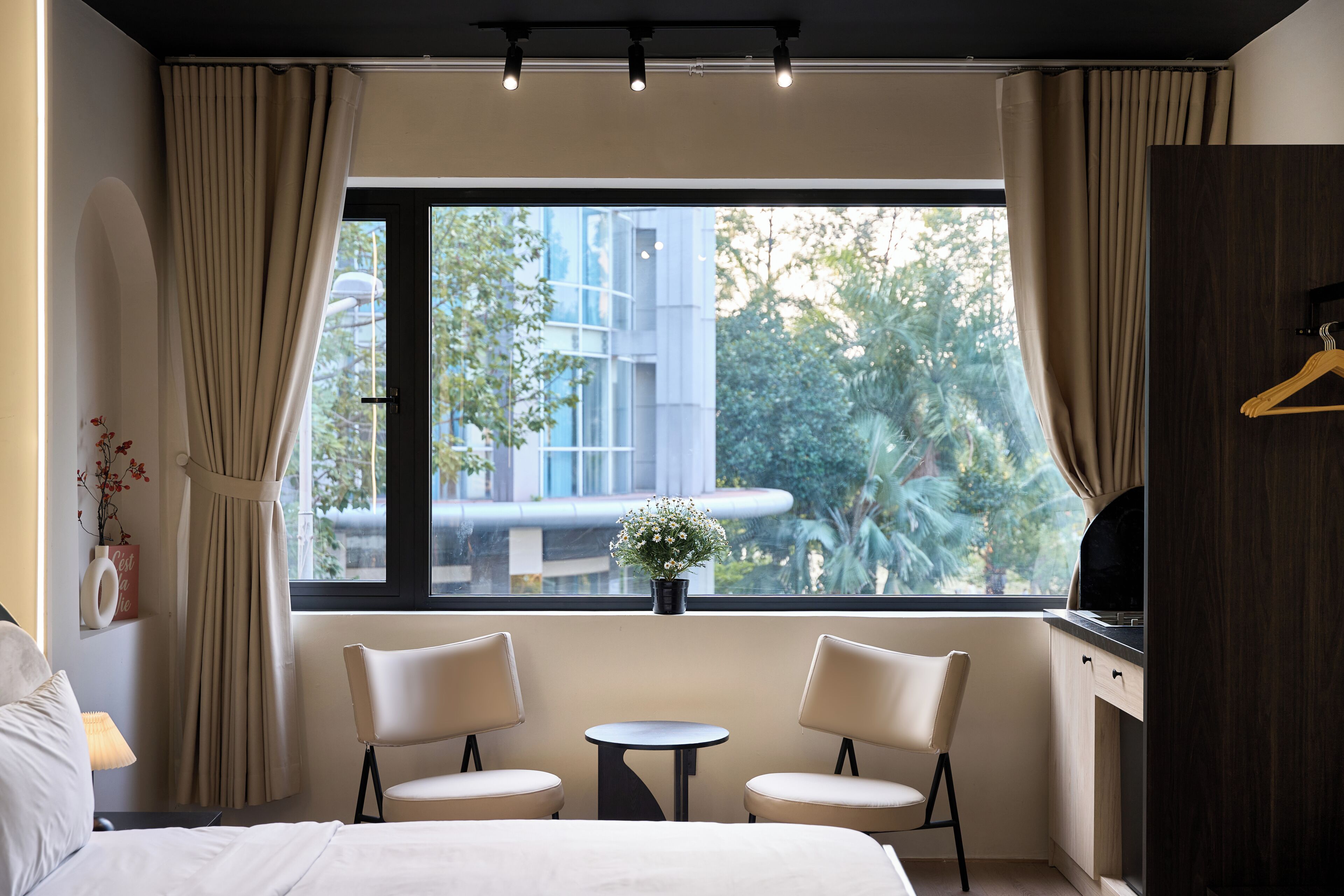 A hotel room with a bed, two chairs, a small table, a TV, and a window with curtains.