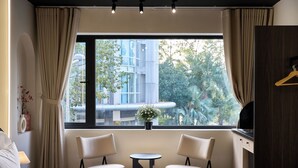 Una habitación de hotel con cama, dos sillones, una mesita, televisor y ventana con cortinas.