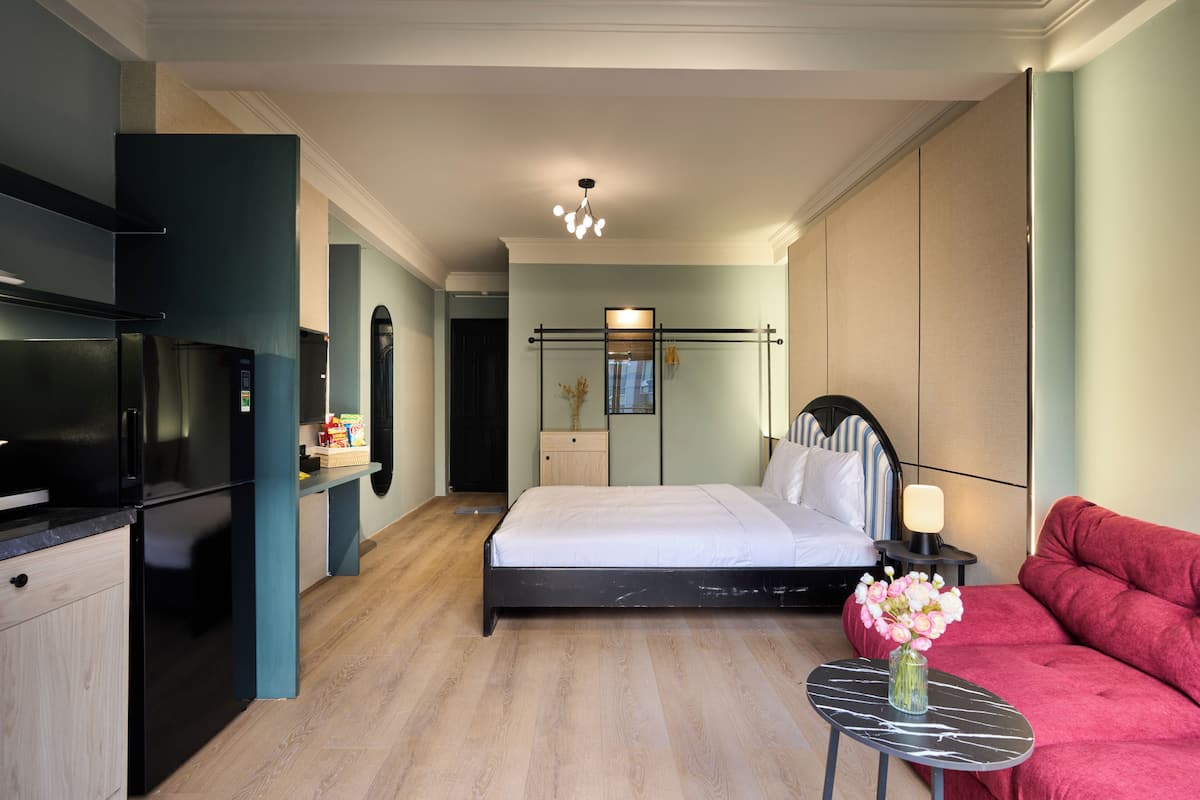 Ein modernes Hotelzimmer mit Bett, einer Couch, einem kleinen Tisch, einem Nachttisch, einem Spiegel und einem eingebauten Kühlschrank.