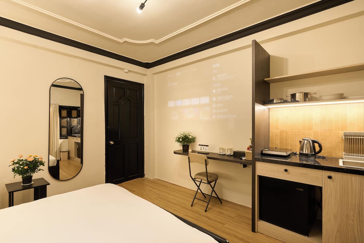 Ein Schlafzimmer mit einem Bett, einem Schreibtisch mit Stuhl, einer kleinen Pflanze, einem Spiegel und einer Projektionsleinwand.
