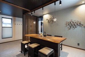 Eine moderne Küche mit einer Holztheke, Barhocker, Pendelleuchten und einem dekorativen Metallkunstwerk an der Wand.