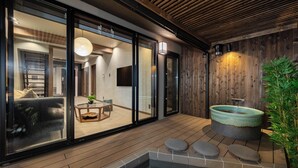 Ein modernes Interieur mit Holzboden, einer Glastür zu einem Wohnbereich und einer Steinsitzbadewanne.