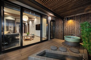 Ein modernes Interieur mit Holzboden, einer Glastür zu einem Wohnbereich und einer Steinsitzbadewanne.