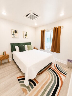 A bedroom with a bed, a nightstand, a window with curtains, and a radiator. - New! The Noir Retreat (Dallas)