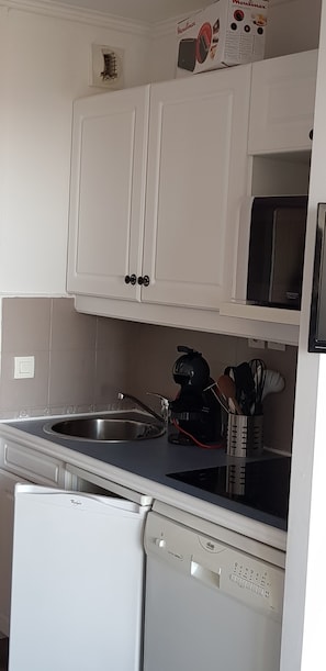 Eine Küche mit weißen Schränken, einer Edelstahl-Spüle, einer Kaffeemaschine und einem Geschirrspüler.