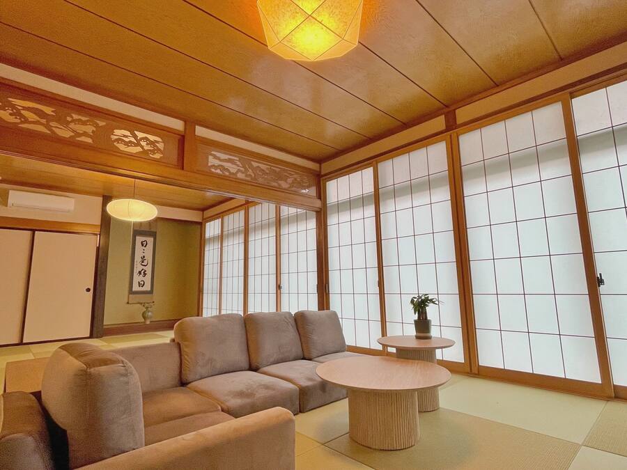 A traditional Japanese room with tatami flooring, a low wooden ceiling, sliding shoji doors, and a sofa.