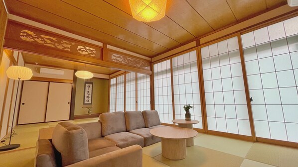Una habitación japonesa tradicional con suelo de tatami, bajo techo de madera, puertas correderas shoji y un sofá.