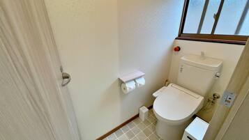 A small bathroom with a toilet, a toilet paper holder, and a window.