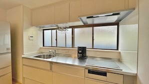 Una cocina con un lavamanos de acero inoxidable, una cafetera y un ventanal con vidrio esmerilado.