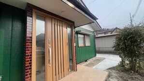 Un edificio residencial con fachada verde, puerta corrediza de vidrio y una ventana pequeña.