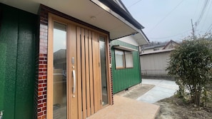 A residential building with a green exterior, a sliding glass door, and a small window. - Tabinoteitaku wa (Sendai-shi)