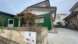 A residential building with a green exterior, a concrete wall with a sign, and a clear sky.