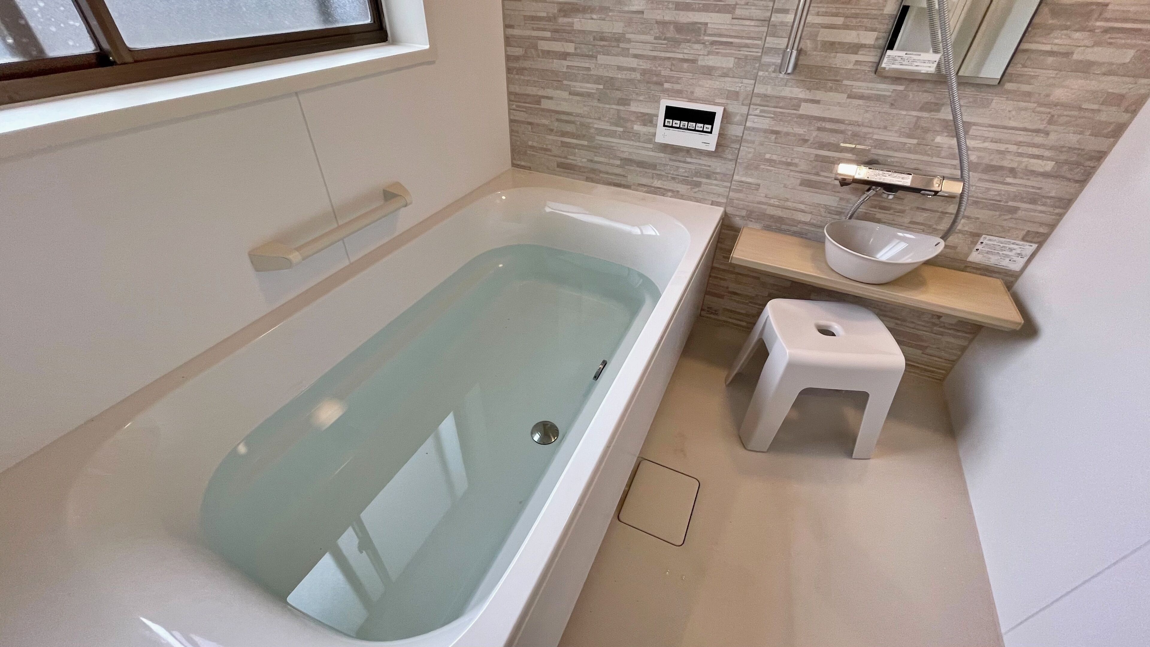 Een moderne badkamer met een badkuip, een klein krukje, een wastafel en een douchepaneel.
