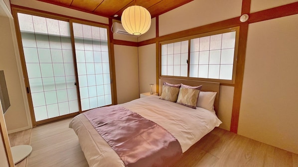 A traditional Japanese-style bedroom with tatami flooring, sliding shoji doors, a bed with a headboard, and a hanging paper lantern.