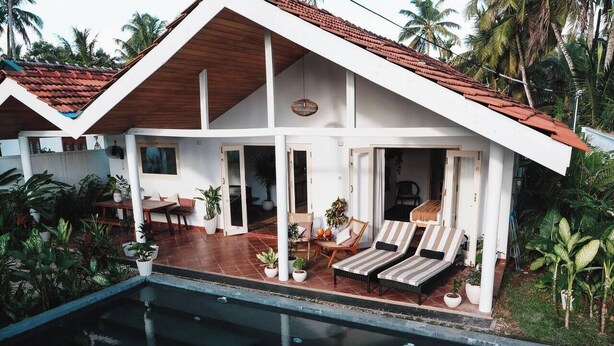 Et hus med pool, overdækket terrasse og udsigt til palmer.
