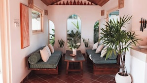 Et hyggeligt rum med træloft, sofaarrangement, et bord og potteplanter.
