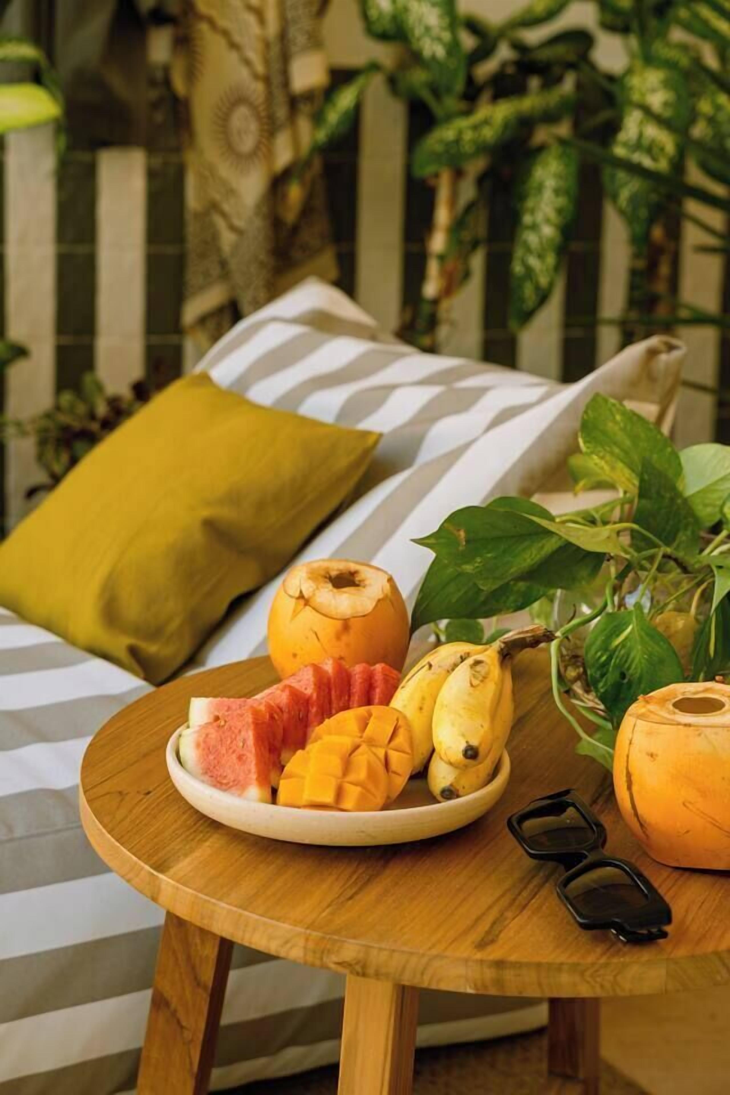 Ein runder Holztisch mit einer Fruchtschale, einem gelben Kissen und einer Pflanze.