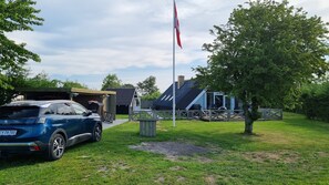 Ein blaues Auto steht auf einer Wiese vor einem Gebäude mit schrägem Dach und Fahnenmast.