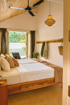 Quarto com cama, ventilador de teto, luminária pendente e vista para o verde lá fora.