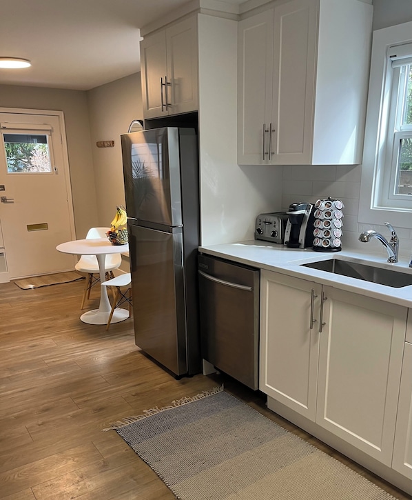 A modern kitchen with stainless steel appliances, a white countertop, and a small dining area.