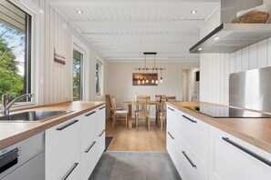 A modern kitchen with white cabinetry, a wooden countertop, a stainless steel refrigerator, and a dining area with wooden chairs and a table. - Spacious cottage close to Enebærodde (Otterup)