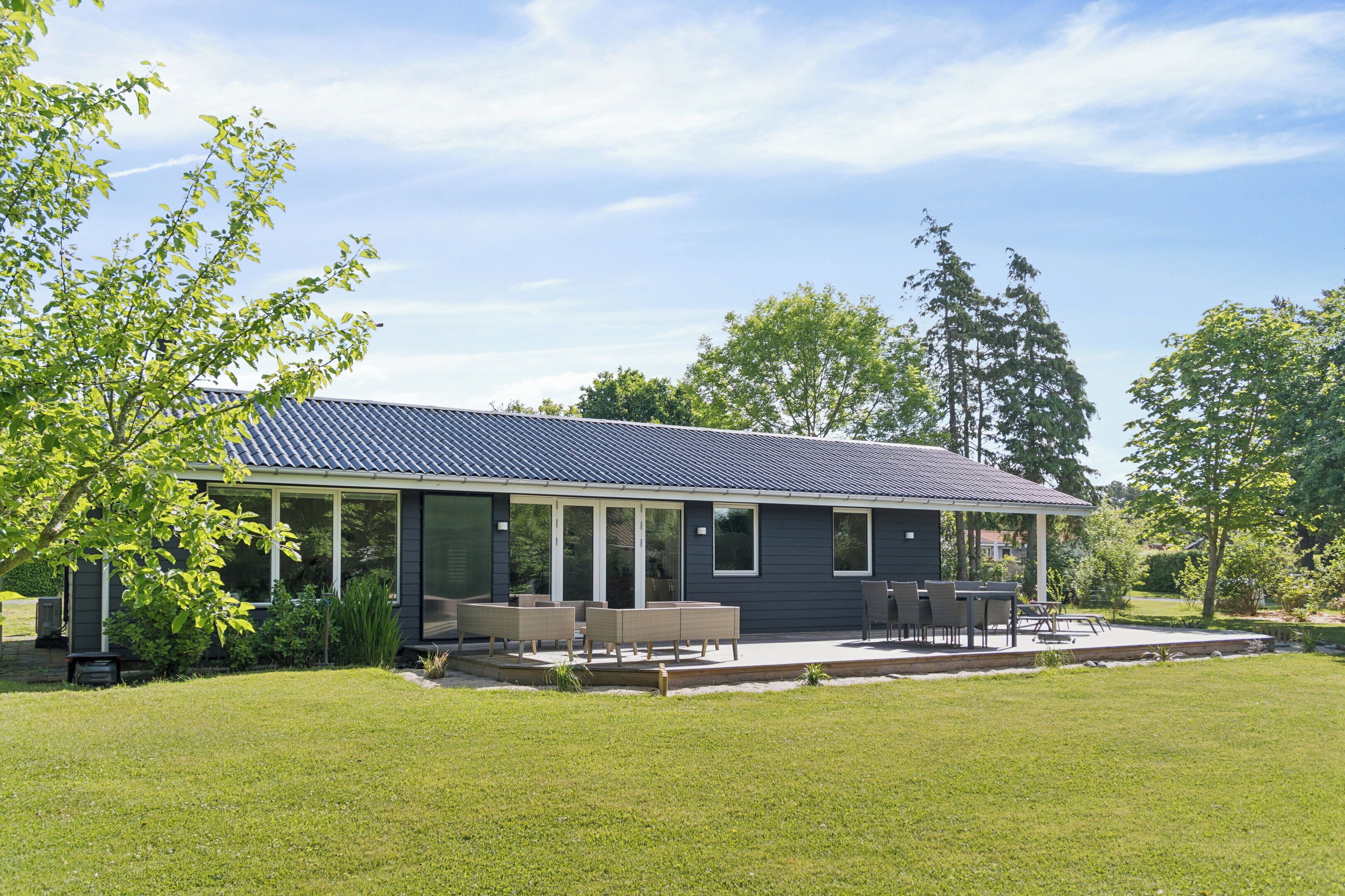 Een modern huis met een overdekte patio, een gazon en bomen op de achtergrond.