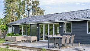 Ett modernt hus med en terrass, utemöbler och stora fönster.