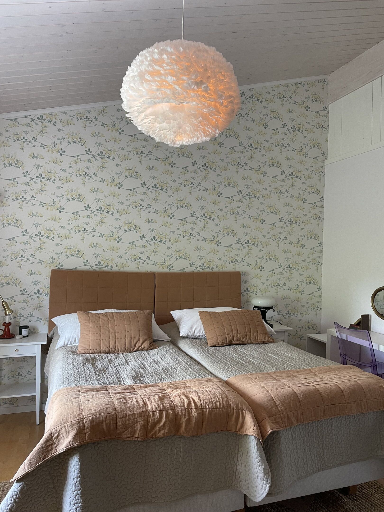 A bedroom with a large bed, a hanging light fixture, a nightstand, and a chair.