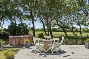 An outdoor patio with a wooden table and chairs, a hot tub, and a garden.