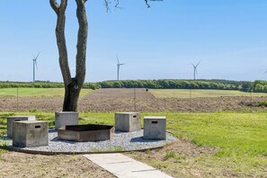 Un parc avec un arbre, des bancs en béton et des éoliennes en arrière-plan.