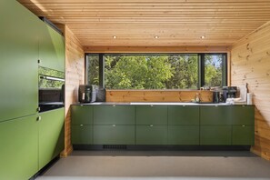 Eine moderne Küche mit grünen Schränken, Holzboden und einem großen Fenster mit Blick auf Grünflächen.