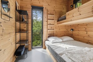 Ein Schlafzimmer einer Holzhütte mit Bett, Regalen und einem Fenster.